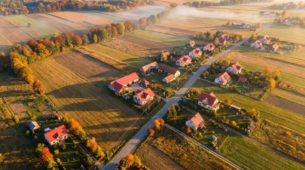 Podkrakowska wieś widziana z drona, skupisko domów jednorodzinnych wzdłuż drogi i pola wokół, ilustracja obszaru uzupełnienia zabudowy